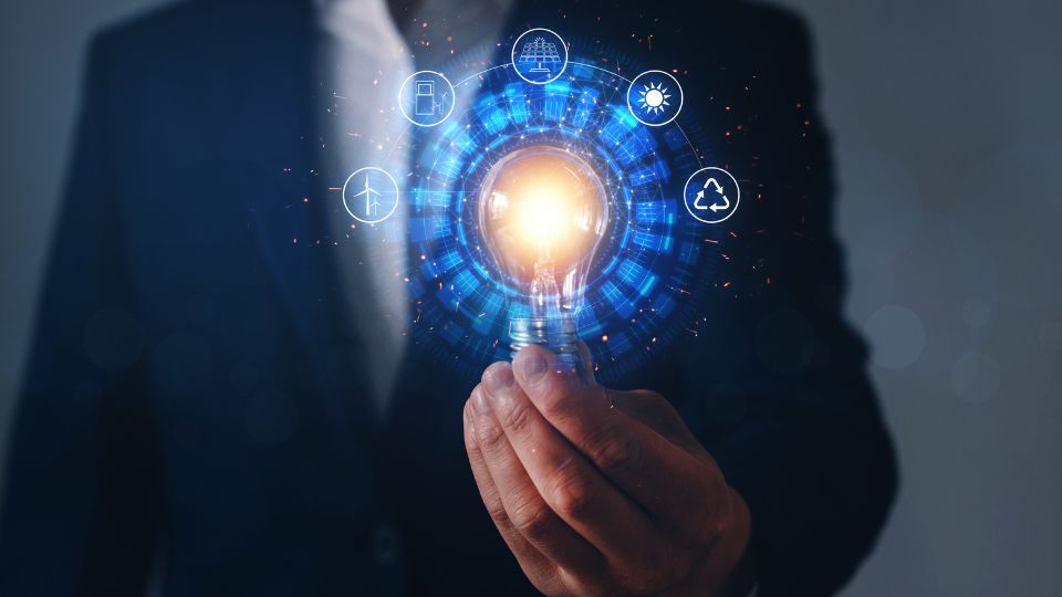 Egy férfi kezében egy világító izzó, amely körül energiahordozók ikonjaival ábrázolt digitális grafika látható.