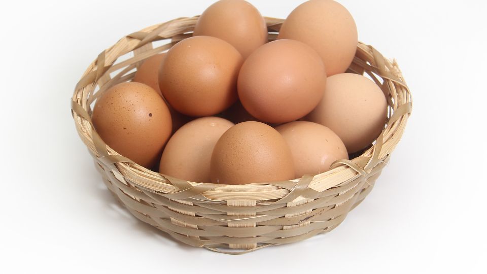 Kerek, barna tojások egy fonott kosárban, fehér háttér előtt.