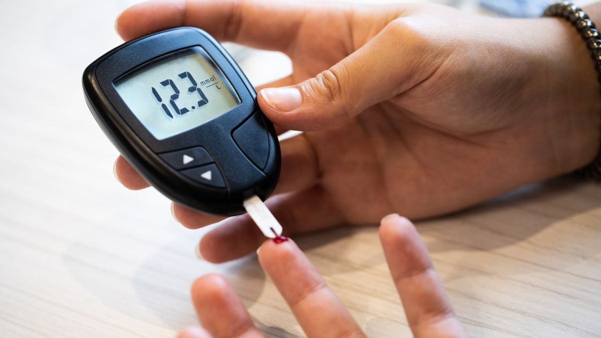 Egy kéz vércukormérőt tart, amelyen 12.3 mmol/l érték látható, vércsepp a mutatóujjon.