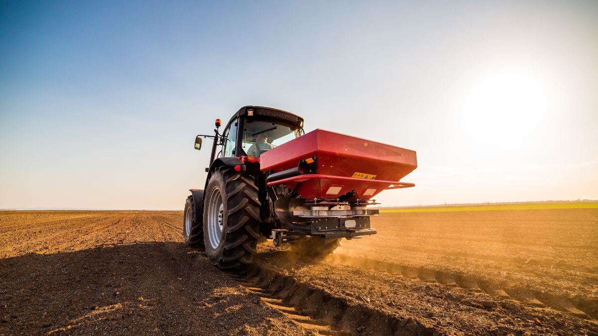 Egy traktor nitrogénműtrágyát szór a földbe, napfényben, mezőgazdasági környezetben.