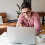 Felnőtt tanuló otthoni környezetben laptop előtt ül, online kurzust néz, koncentrálva.